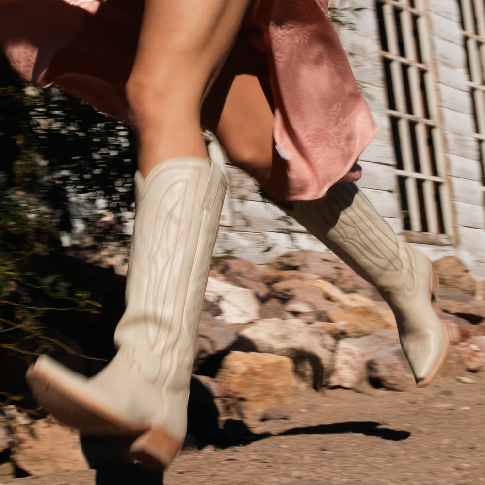 Person wearing white knee-high boots walking on a rocky path with a blurred background