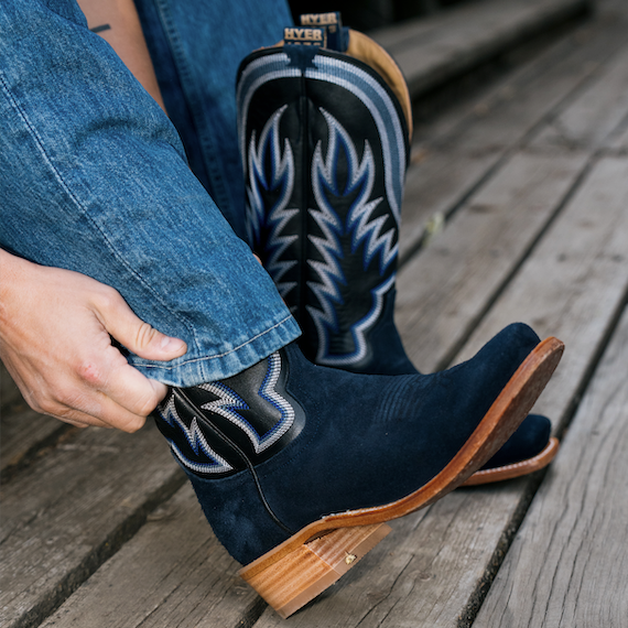 Man pulling jeans down over navy and black cowboy boots with wood decking background