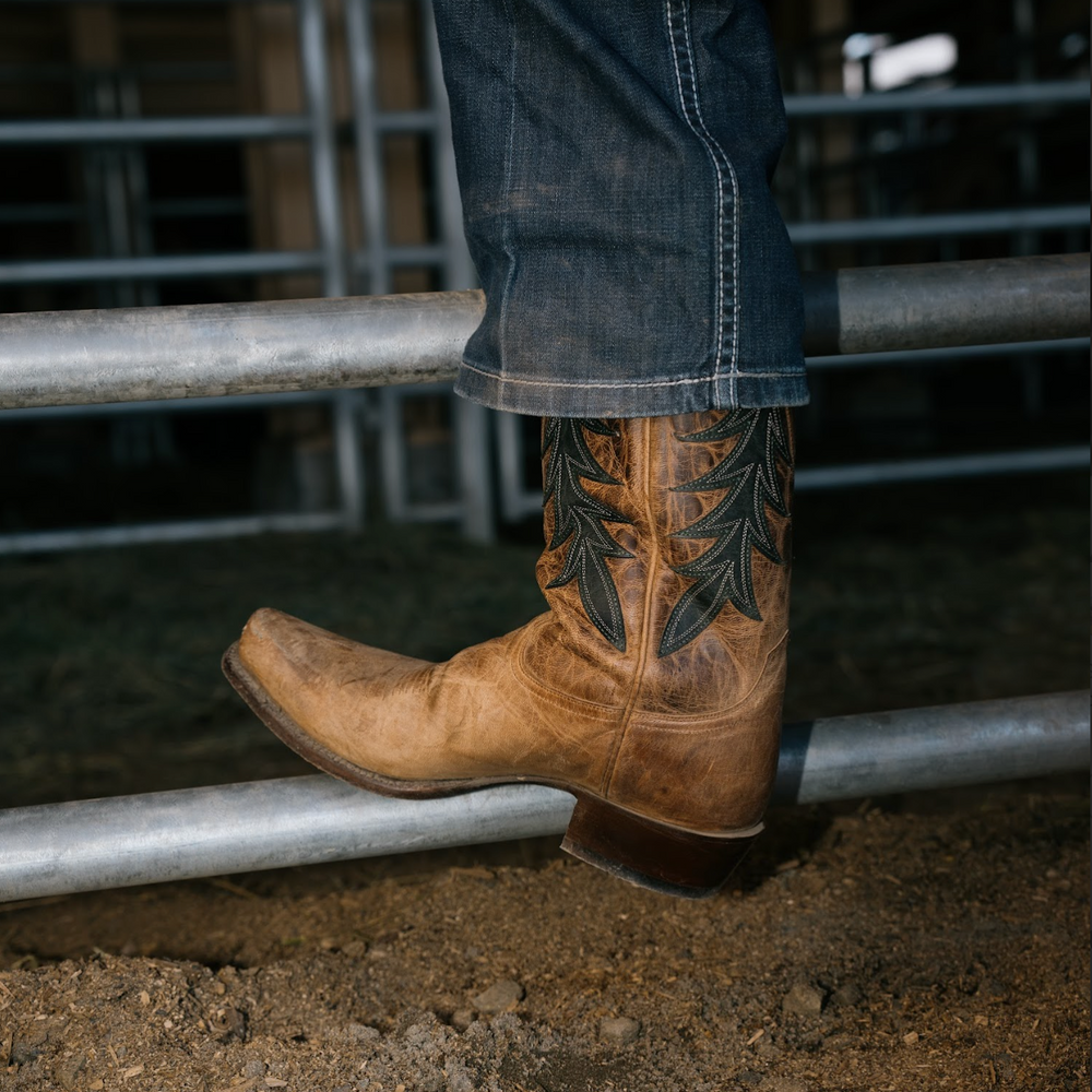Brown cowboy boot with intricate design on a metal gate.